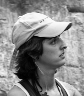 black & white head shot of dark haired woman in a baseball cap looking to the right.