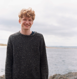 young man in a black jumper with short wavy red hair