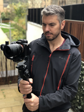 man with short beard holding a camera on a tripod.