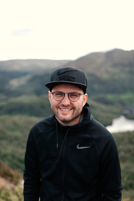 colour photo of caucasian young man wearing black baseball cap.