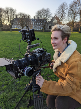 young woman in a sheepskin coat with short blond hair operating a cine camera