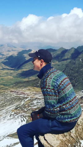 young man in baseball cap at the top of mountains 