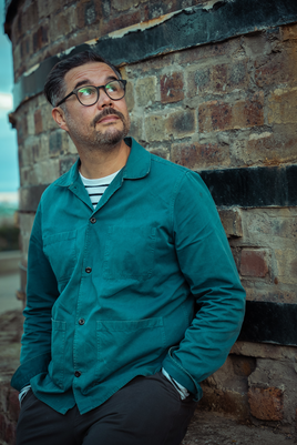 young man with goatee beard and glasses standing against a brick wall.