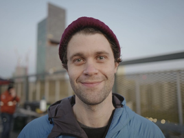 young caucasian man in a red beany hat and blue jacket smiling.